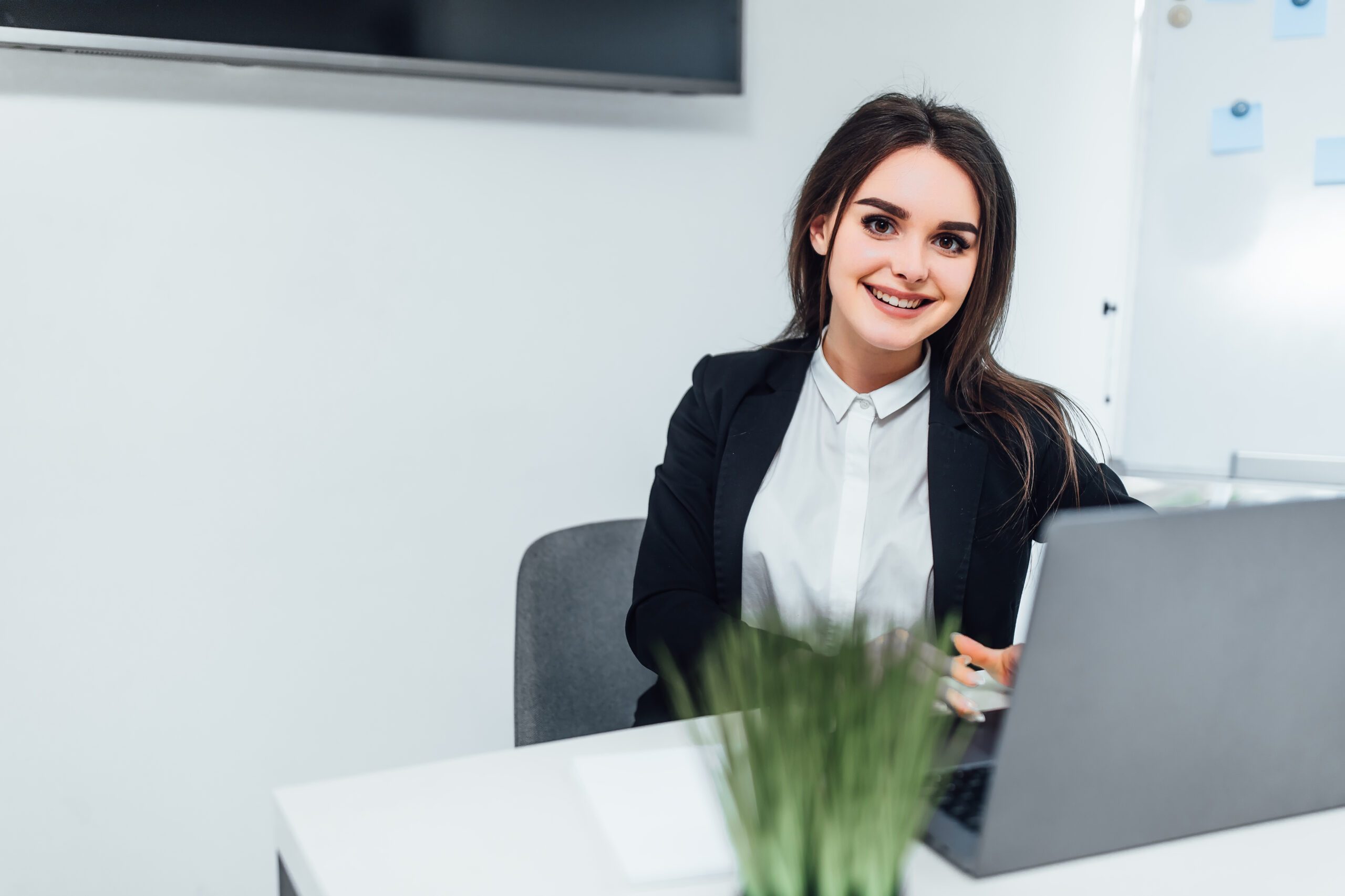 Smiling businesswoman dressed casual suit sitting in modern office and using laptop. With copy space..